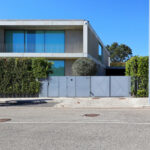 Eduardo Souto de Moura’s Utopia Villa 7 showcasing a modern design with clean lines, large glass windows, and a sleek car door and rear-view mirror of a classic personal luxury car visible in the foreground.