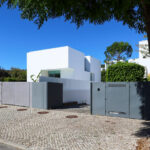 Francisco Aires Mateus’s Utopia Villa 1 showcasing a minimalist concrete and plaster façade with composite material accents, shaded balconies, and a modern gate.