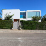 Francisco Aires Mateus’s Utopia Villa 1 showcasing a minimalist design with extensive daylighting and a neatly trimmed hedge surrounding the modern structure.