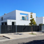 Unknown Architect’s Utopia Villa 12 showcasing a modern residential area with composite material construction, a gated entrance, fence, and suburban home fencing along a tar driveway.