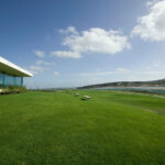 Gonçalo Cardoso de Menezes’ Former Sales Office, Lot 165, showcasing a minimalist structure set within an expansive agricultural field with a plain lawn and open hinterland surroundings.