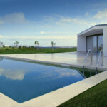 Álvaro Siza Vieira’s 14 Architectural Villas, Lot 1, showcasing a composite material façade with a reflecting pool, swimming pool, landscaped lawn with artificial turf, and integrated water features enhancing daylighting.