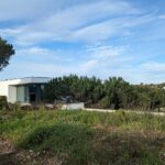 Alcino Soutinho’s 10 Architectural Villas, Lot 240, showcasing modern villas with clean lines, flat roofs, and integration with surrounding green vegetation and shrubland under a clear blue sky.