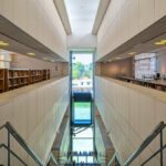 Alcino Soutinho’s Biblioteca Municipal Florbela Espanca interior showcasing symmetrical shelving made of metal and composite materials, extensive glass panels allowing natural daylighting, and a modern engineered design.