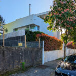 Alcino Soutinho’s Cavadas Santos Residence showcasing a modern suburban home with a clean-lined façade, surrounded by a manicured hedge, driveway with a subcompact car, and visible overhead power lines.