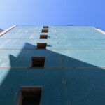 Alcino Soutinho’s Conjunto Habitacional Palácio da Enseada showcasing a high-rise building with a composite material façade, extensive glass panels, and modern engineering elements under a clear blue daytime sky.