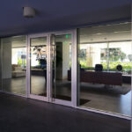 Alcino Soutinho’s Conjunto Habitacional Palácio da Enseada showcasing an interior with composite material flooring, concrete walls, metal-framed glass doors, and a ceiling with integrated shading elements.