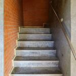 Alcino Soutinho's Department of Ceramics and Glass Engineering at the University of Aveiro showcasing a modern design with concrete and composite materials, featuring prominent stairs with a silver handrail and a brown wood-stained floor.