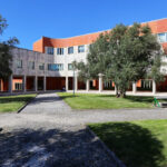 Alcino Soutinho's Department of Ceramics and Glass Engineering at the University of Aveiro showcasing a modern facade with expansive glass panels, surrounded by a landscaped lawn and shaded areas on the academic campus.