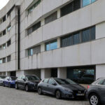 Alcino Soutinho’s Edifício Delfim Pereira da Costa showcasing a modern commercial condominium with a multi-level parking lot filled with various cars, featuring clean lines and a functional glass façade.