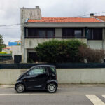 Alcino Soutinho’s Habitação unifamiliar em Matosinhos showcasing a modern residential design with clean lines, large glass windows, and a minimalist façade, featuring a car parked in front with visible automotive exterior elements.