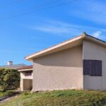 Alcino Soutinho's Holiday House in Praia de Suave-Mar showcasing a modern residential design with a prominent wall and roof structure, set in a rural area with a spacious land lot.