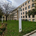 Alcino Soutinho's Matosinhos Town Hall showcasing a modern urban design with a prominent glass façade, surrounded by a well-maintained lawn and shaded areas, set against a backdrop of daytime urban settlement.