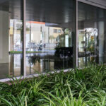 Alcino Soutinho’s design of Quinta das Sedas showcasing a commercial headquarters with a transparent glass façade, composite materials, extensive daylighting, and integrated shade elements surrounded by houseplants.