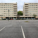 Alcino Soutinho’s Quinta das Sedas featuring a modern condominium complex with high-rise apartment buildings, glass façades, and integrated parking areas along an asphalt thoroughfare in an urban setting.