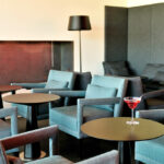 Nuno Graça Moura’s Tennis Club, Lot 161 interior showcasing modern furniture with wooden flooring, sleek tables and chairs, a coffee table, and a stylish living room area with armrests.