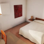 Eduardo Souto de Moura’s Convento das Bernardas Residence interior showcasing wooden flooring, brown wooden ceiling beams, minimalist furniture, and a warm, spacious bedroom with natural light.