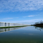 Nuno Graça Moura’s 30 Architectural "Bar Code 1" Townhouses, Lot 152, showcasing a modern design with reflective glass façades overlooking a serene reflecting pool and wetland reservoir.